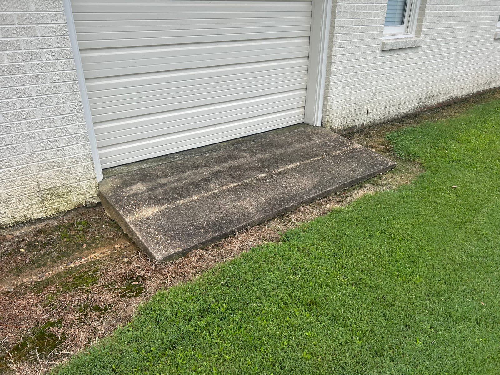 Algae-stained concrete apron at a garage door before pressure washing